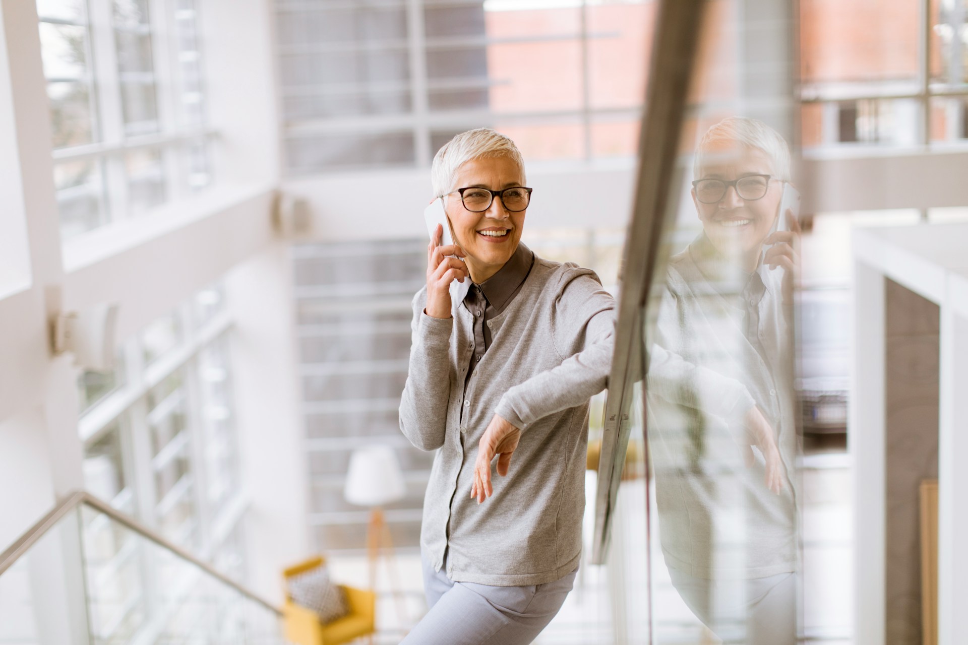 Una donna appoggiata alla balaustra di una scala sorride mentre parla al telefono